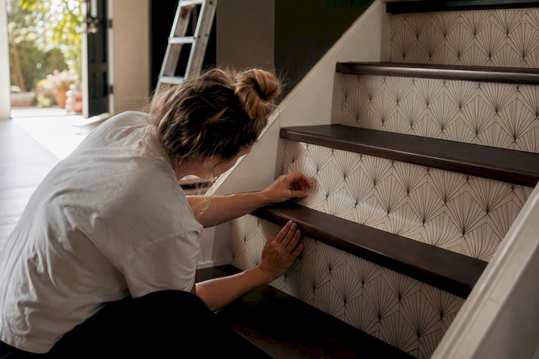 Hands smoothing wallpaper on staircase riser